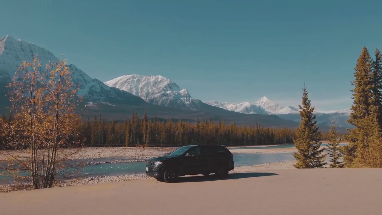 Black Jeep Grand Cherokee parked by a glacial river with the Canadian Rockies in the background